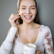 Smiling woman putting cream on her face looking at camera