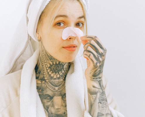 Tattooed woman in bathrobe removing nose patch