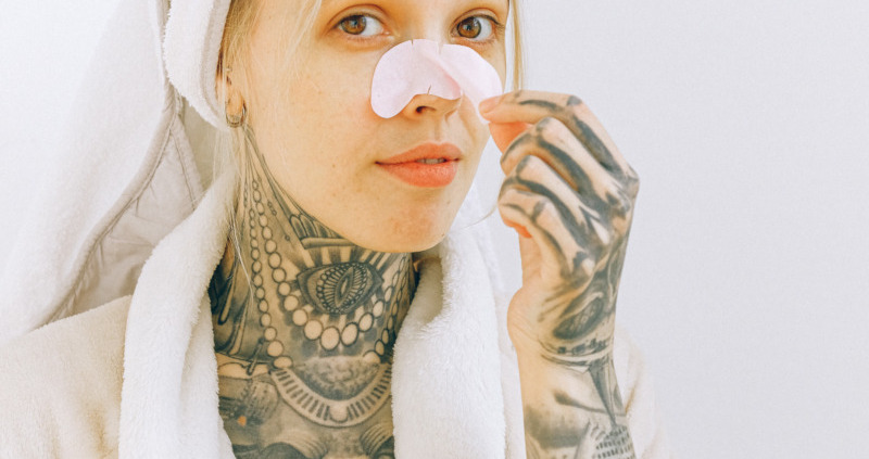 Tattooed woman in bathrobe removing nose patch