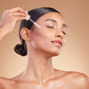 Woman, dropper and retinol on face for skincare beauty or cosmetics against a studio background. Beautiful female with pipette applying oil drop to skin for hydration, moisturizer or facial treatment