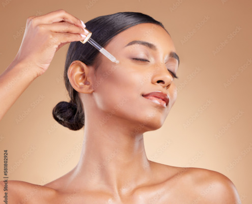 Woman, dropper and retinol on face for skincare beauty or cosmetics against a studio background. Beautiful female with pipette applying oil drop to skin for hydration, moisturizer or facial treatment